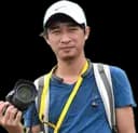 Hong Makara, smiling, with a camera and a cap
